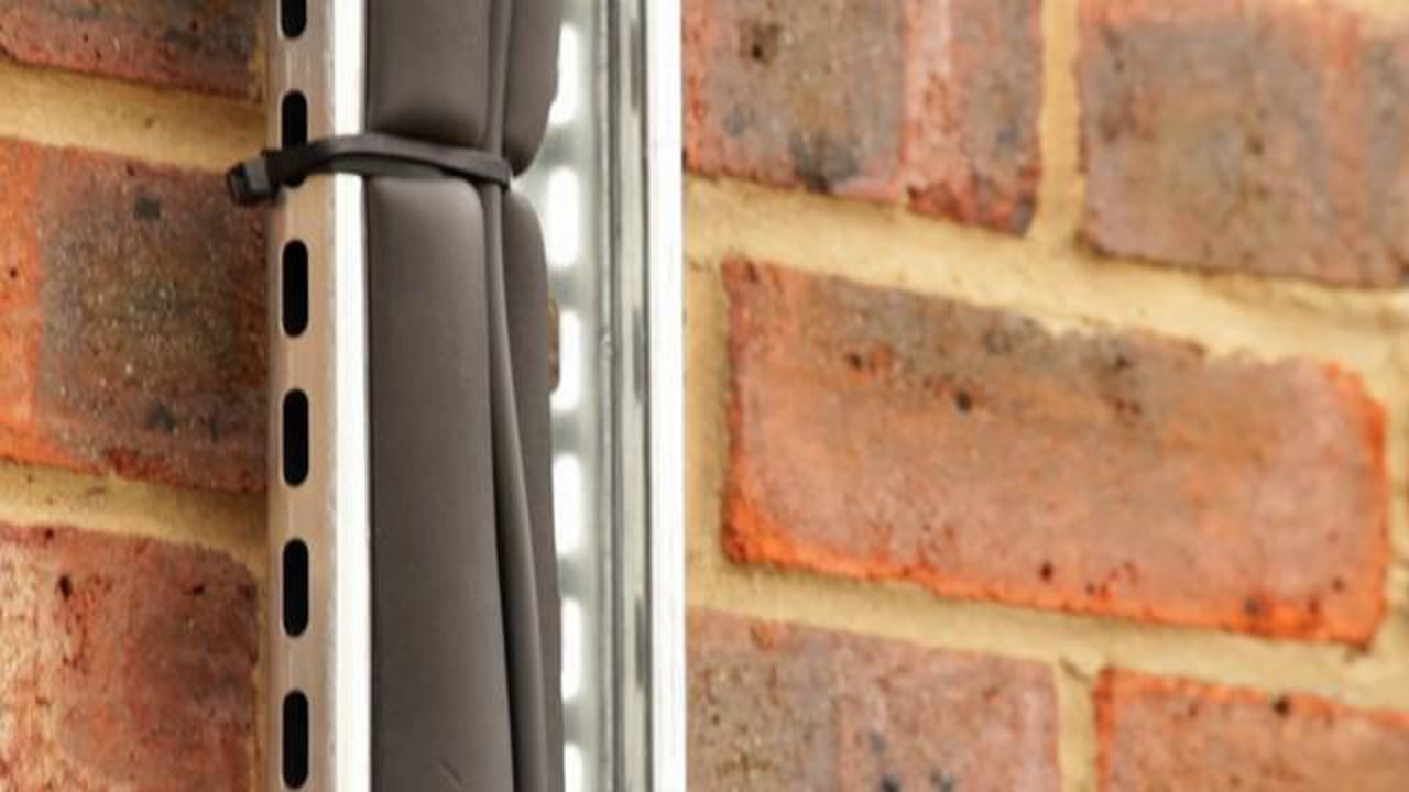 Dark Exo Shield cable secured vertically beside metal channel and a brick wall.