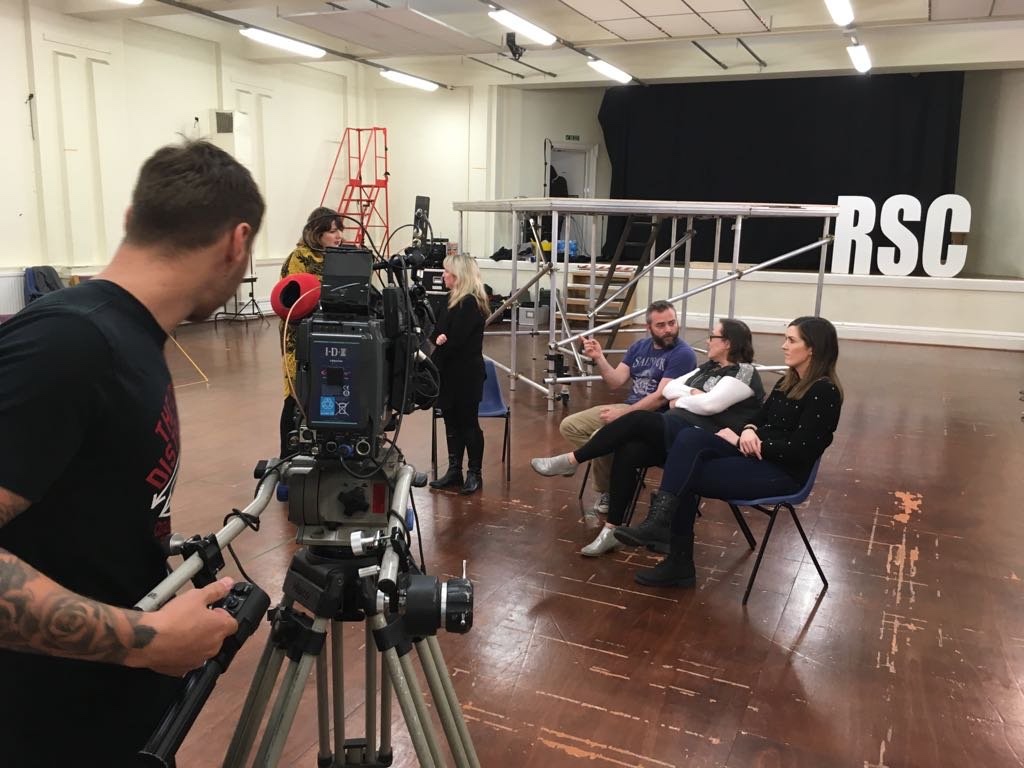 Camera operator filming three seated contributors beside large RSC letters in the Romeo and Juliet rehearsal room.