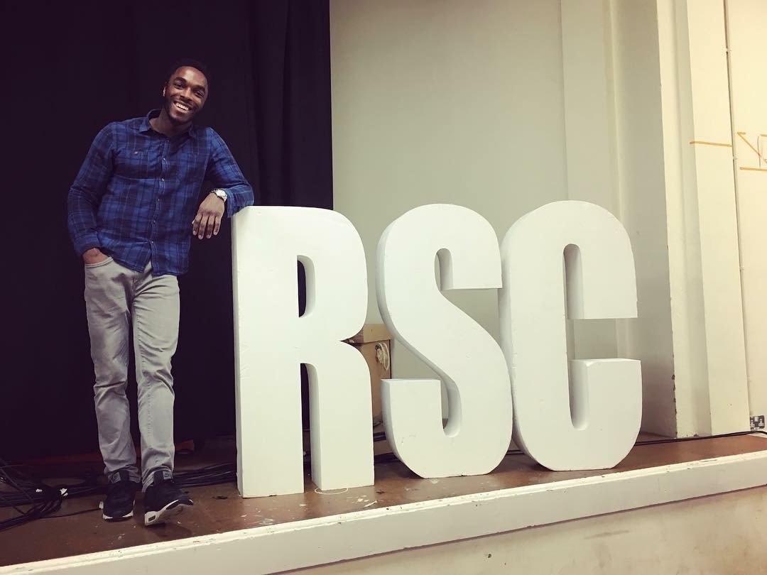 Romeo and Juliet cast member standing beside large RSC letters in the rehearsal room.