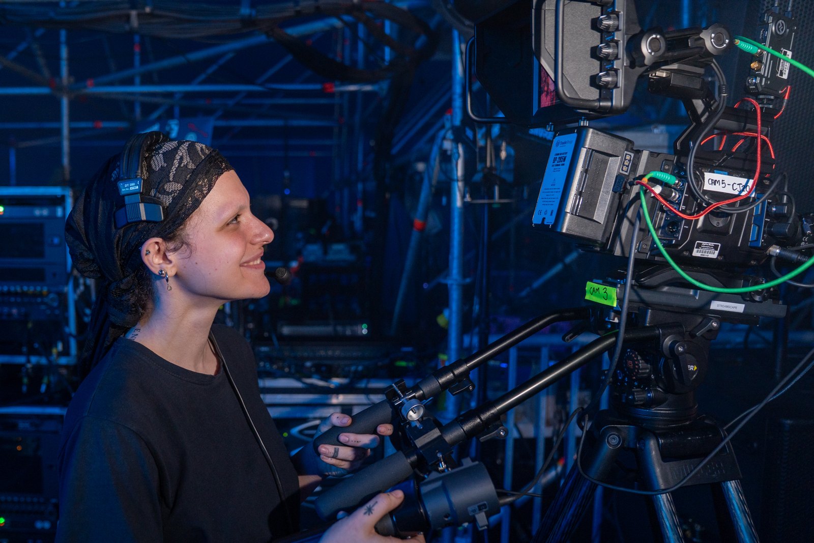 Smiling camera operator working beside a broadcast camera at Reminisce festival